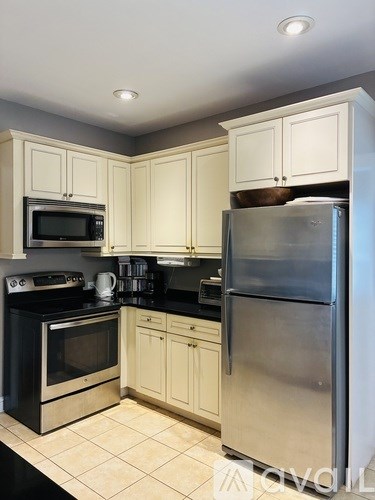 A kitchen with a stainless steel refrigerator, black oven, and white cabinets.