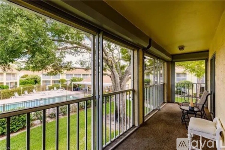 A balcony with a table and chairs overlooking a pool and greenery.