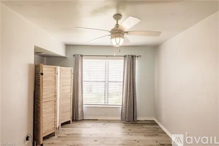 A room with a ceiling fan and a window with curtains.