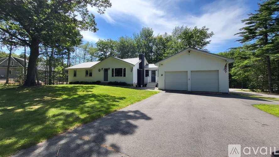 A house with a white exterior is surrounded by greenery and has a driveway leading to the garage.