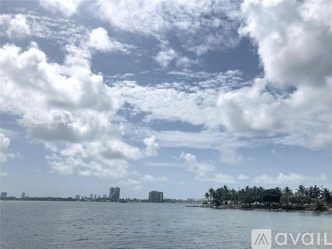 A body of water with buildings and trees in the distance under a cloudy sky.
