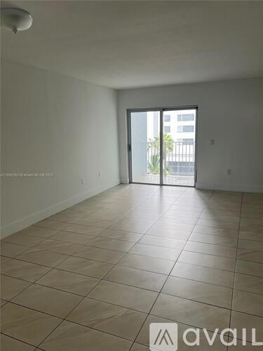 A large empty room with tiled flooring and a sliding glass door leading to a balcony.