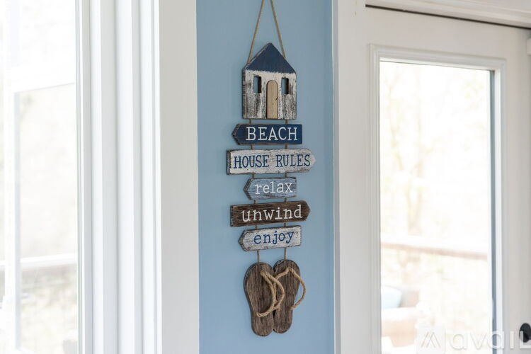 A sign that says beach house rules with a house and rope hanging from it.
