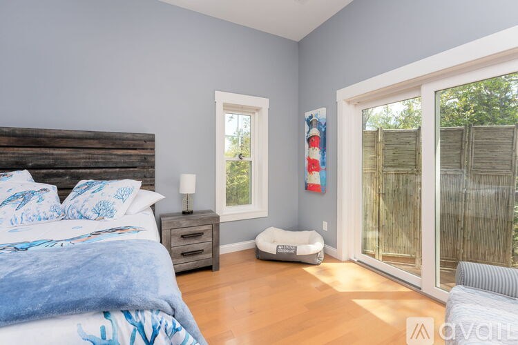 A bedroom with a bed, nightstand, and a window with a view of a fence.