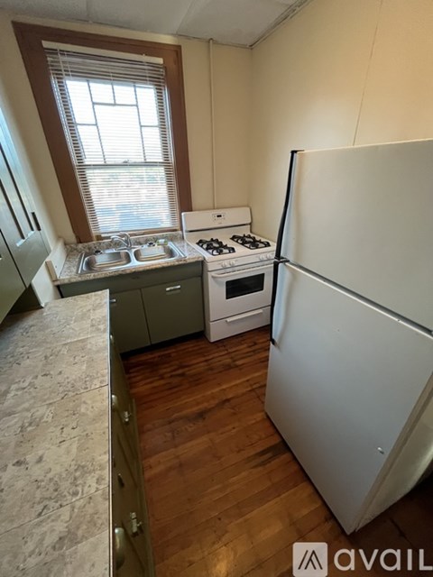 A kitchen with a white fridge, a white stove, and a window with blinds.