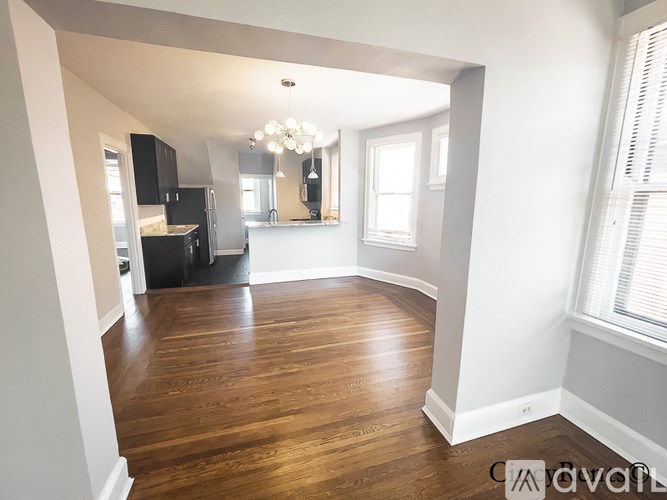 A large empty room with wooden floors and a kitchen area in the background.