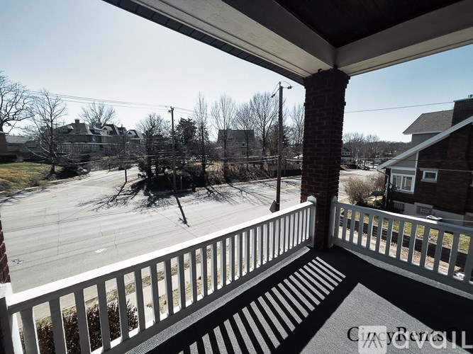 A porch with a white railing and a view of a street and houses.