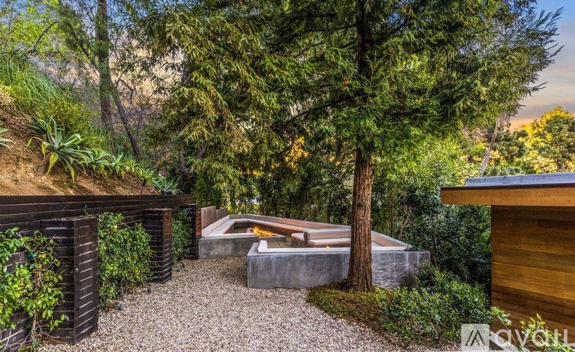 A backyard with a bench, a fire pit, and a tree.