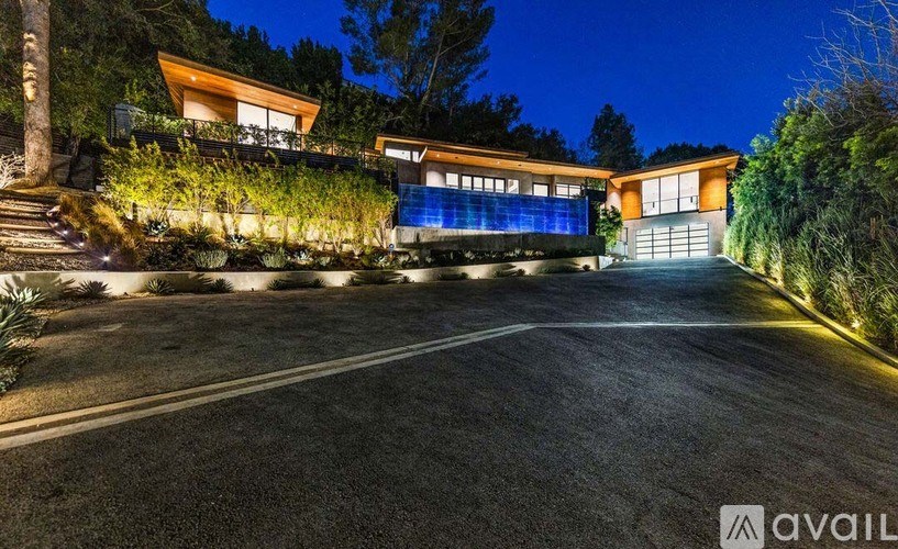 A modern house with a driveway and garage is illuminated at night.
