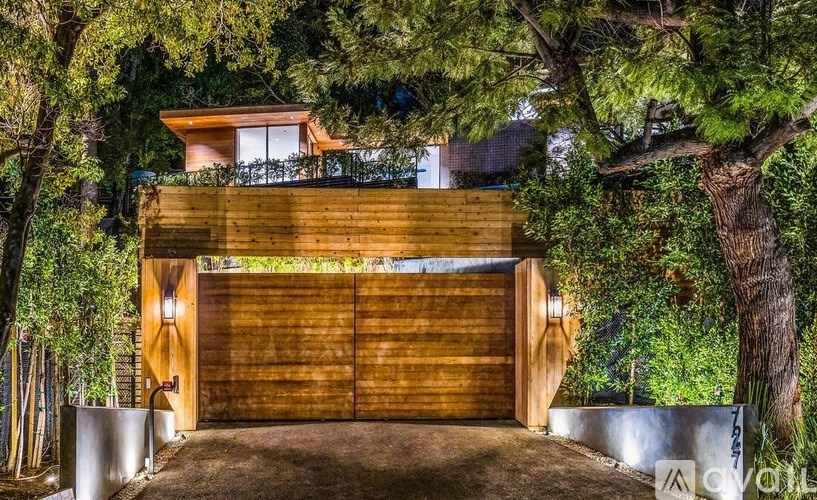 A modern house with a wooden garage door is surrounded by trees.