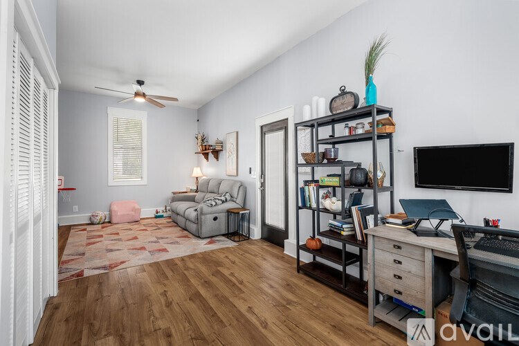 A room with a ceiling fan, a couch, a chair, a desk with a laptop, and a bookshelf.