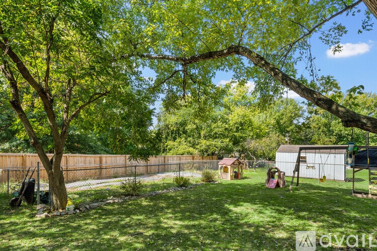 A tree with green leaves is in the foreground of a sunny backyard.
