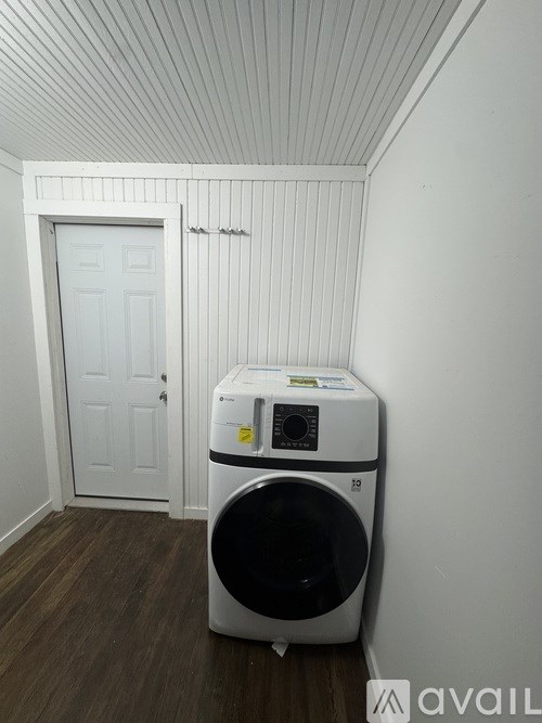 A white washing machine sits in a small room with a door in the background.