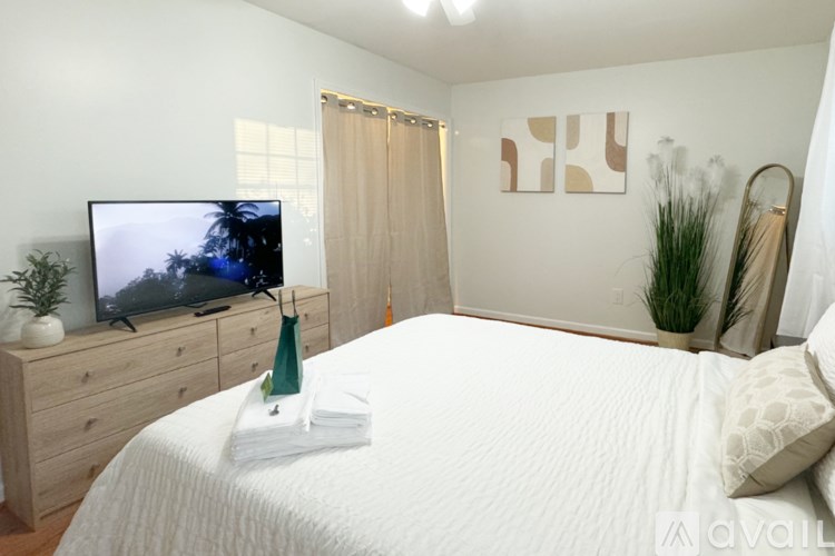 A bedroom with a bed, a TV, and a plant.