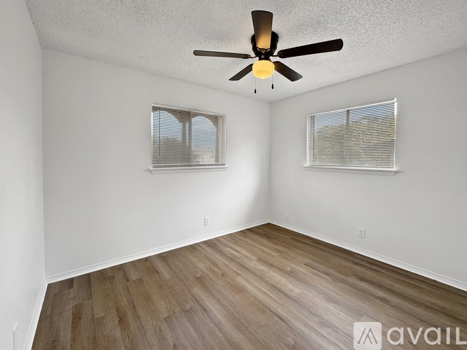 A room with a ceiling fan and two windows.
