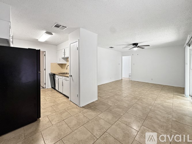 A black refrigerator is on the left in a kitchen with white cabinets and a fan in the ceiling.