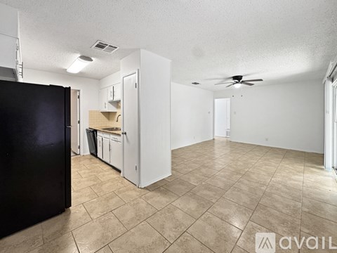 A black refrigerator is on the left in a kitchen with white cabinets and a fan in the ceiling.