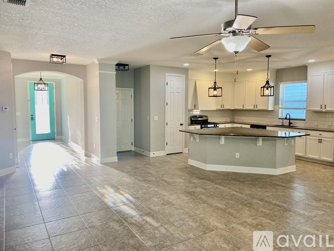 A spacious kitchen and living room with a fan and lighting fixtures.