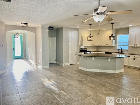 A spacious kitchen and living room with a fan and lighting fixtures.