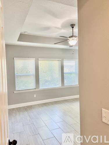 A room with a ceiling fan and three windows.