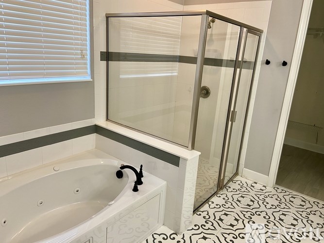 A white bathtub with a black faucet is in a bathroom with a glass shower door.