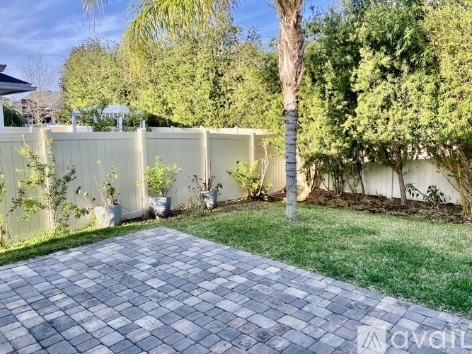 A backyard with a paved walkway and a white fence.