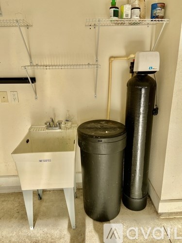 A white sink with a black trash can and a green gas cylinder.