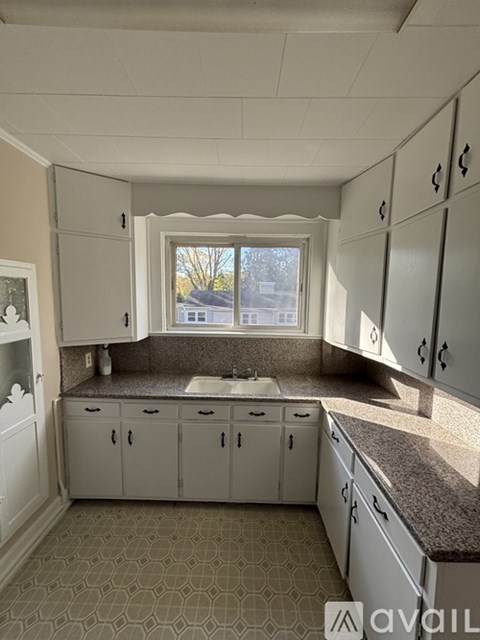 A kitchen with white cabinets and a window overlooking a house.
