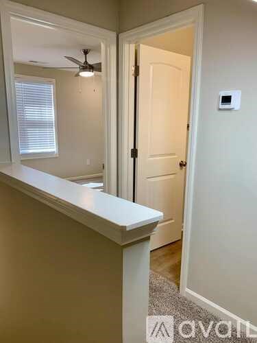 A white door is open to a hallway with a fan and light switch on the wall.