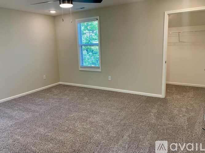 A room with a carpeted floor, a window, and a ceiling fan.