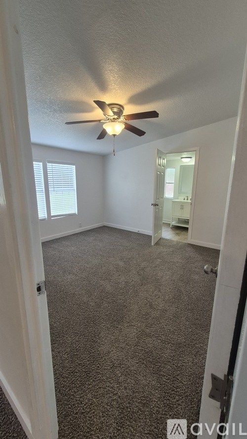 A carpeted room with a ceiling fan and a door leading to another room.