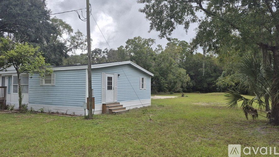 A blue house with a white door and a porch is surrounded by greenery.