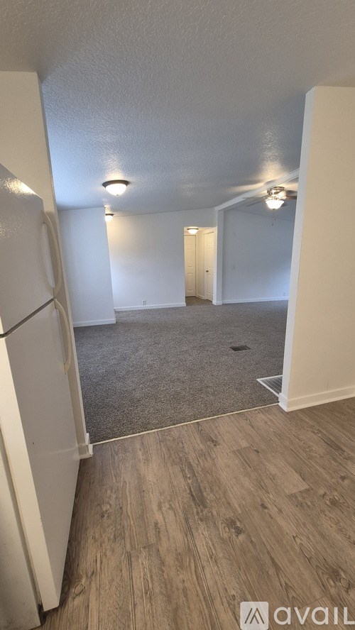 A room with a white fridge and wooden flooring.
