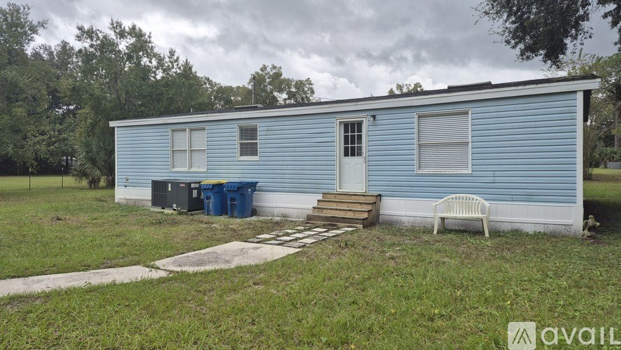 A blue house with a white door and windows is surrounded by greenery.