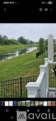 A river flows through a green landscape with a white fence and a white pillar in the foreground.