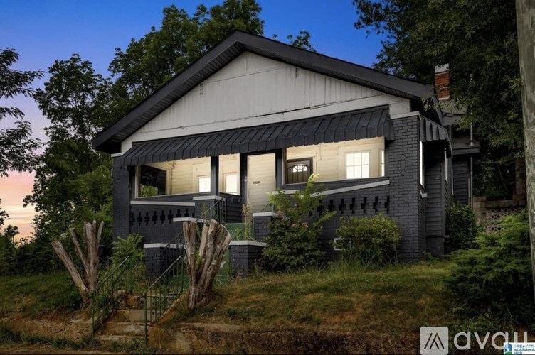 A house with a dark grey exterior and a black roof is surrounded by greenery.