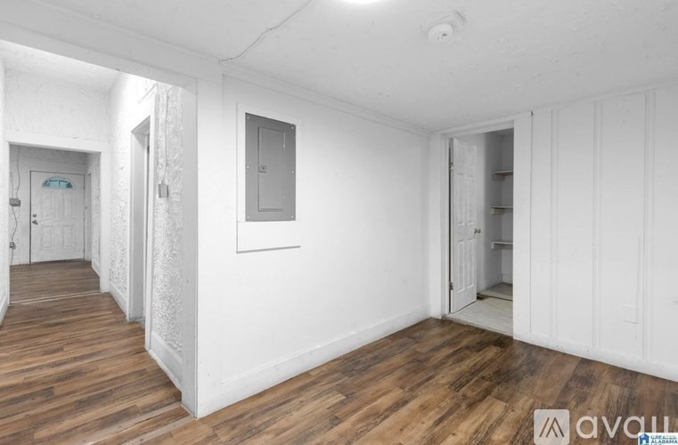 A room with wooden floors and white walls, with a door on the left and a partially open door on the right.