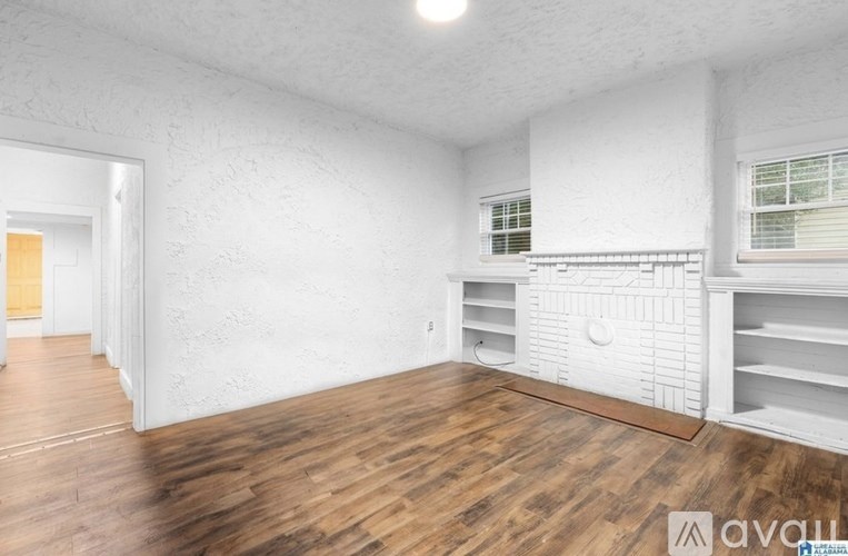 A room with white walls and wooden flooring, with a window and a door visible.