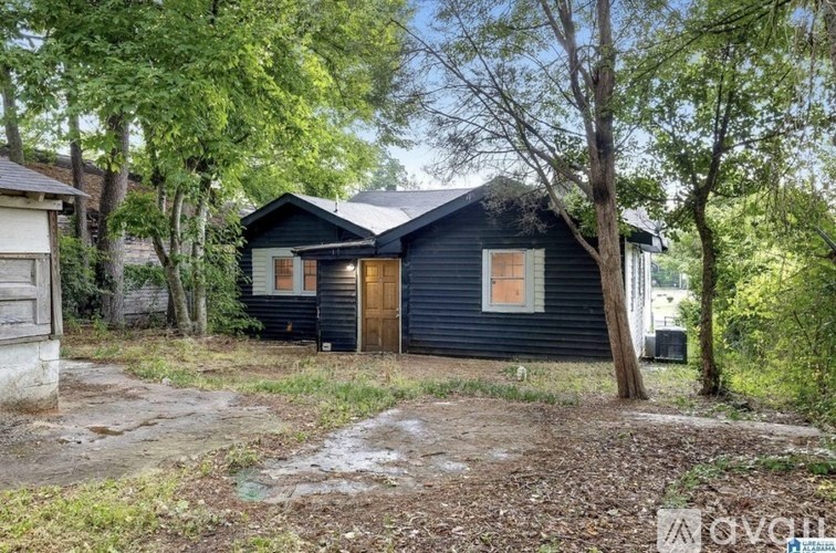 A black house with a brown door is surrounded by trees and grass.