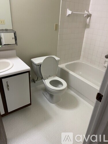A white toilet sits in a bathroom next to a sink and a bathtub.