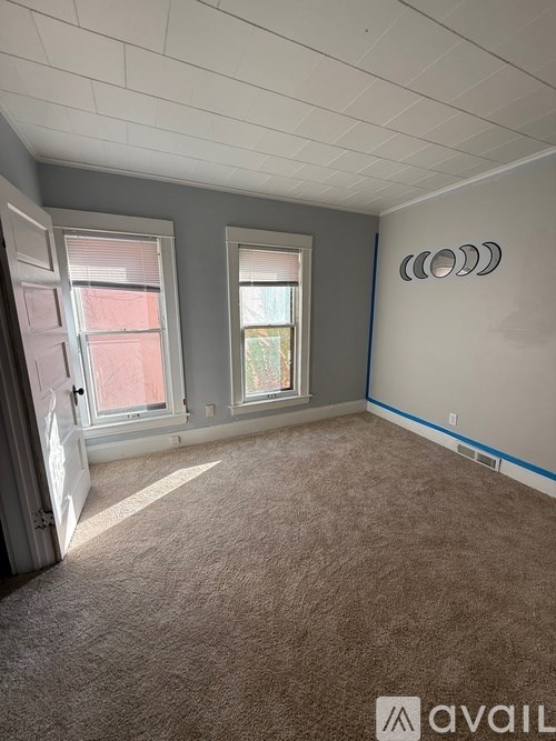 A room with carpeted floor, two windows, and a wall with a logo.