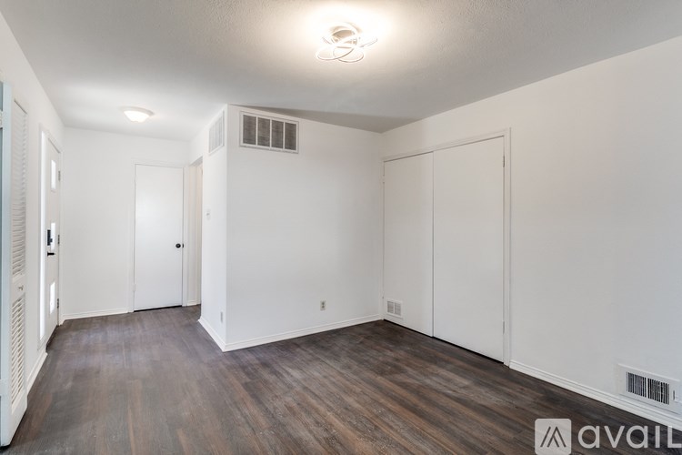 A room with wooden floors and white walls, with a door on the left and a window on the right.