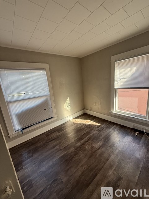 A room with wooden flooring and two windows.