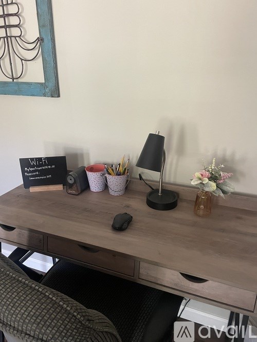 A wooden desk with a mouse, a lamp, a cup of pens, a small vase with flowers, and a sign that says "Wi-Fi".