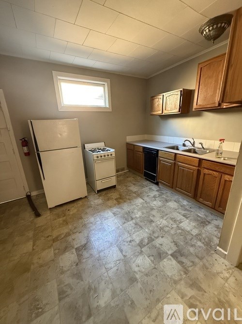 A kitchen with a white fridge, wooden cabinets, and a tiled floor.