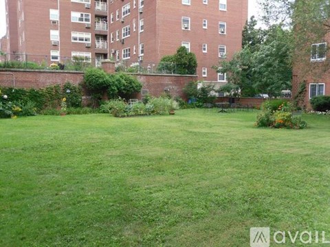 A grassy area in front of a brick building with a wall and bushes.