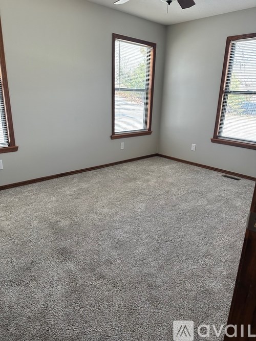 A room with grey carpet and two windows.