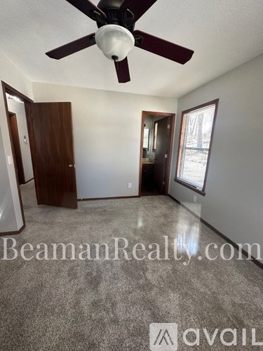 A room with a ceiling fan and a window with a view of trees outside.