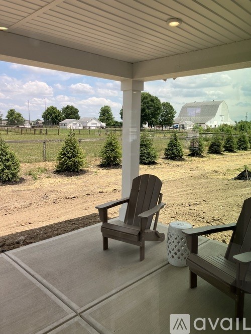 A wooden chair is on a porch with a view of a field and a barn.