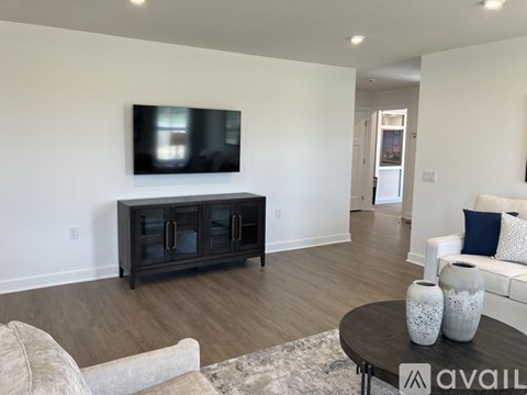 A living room with a grey sofa, a black cabinet, and a television mounted on the wall.